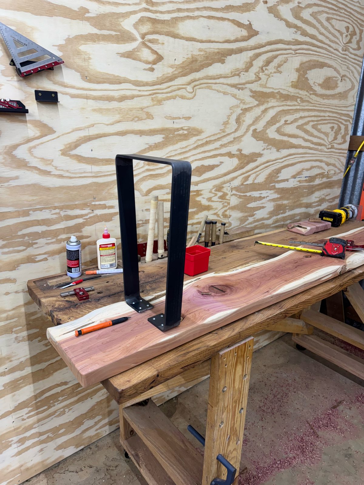 Live-edge eastern red cedar bench top on the workbench with a black steel hairpin-style leg being fitted