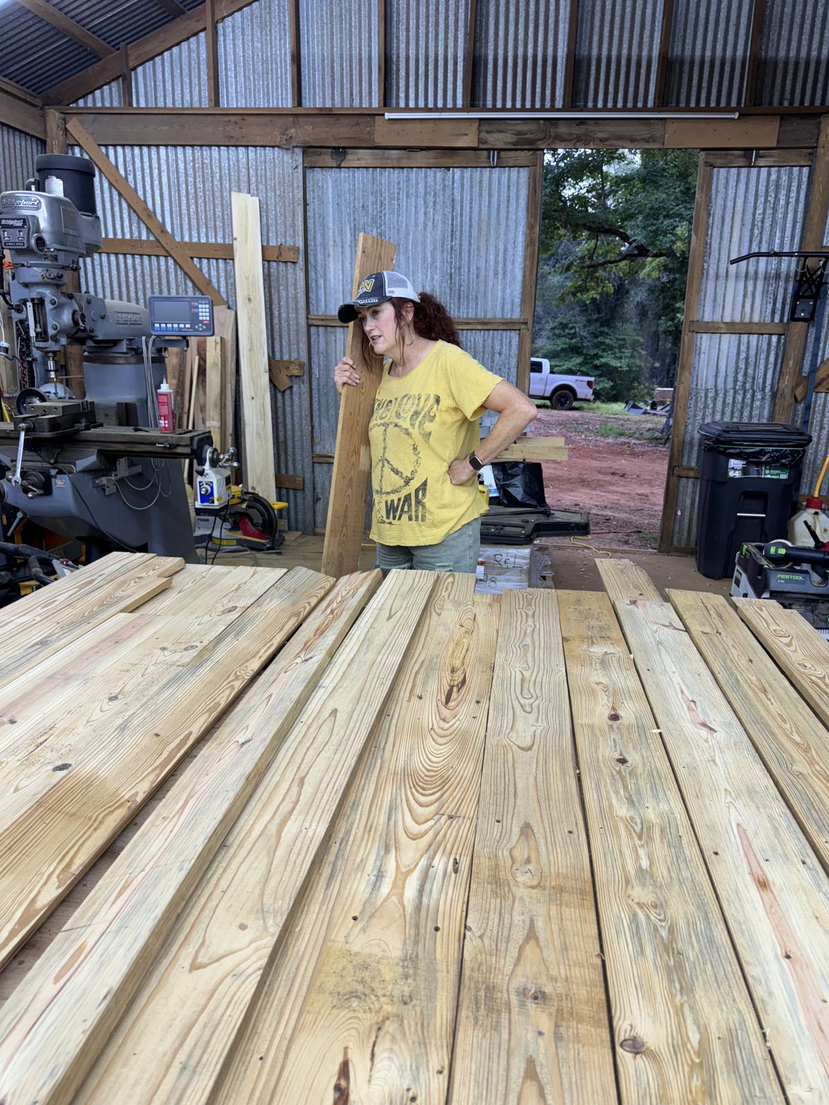 Carrying a board through the shop past rough-sawn pine boards laid out on the floor
